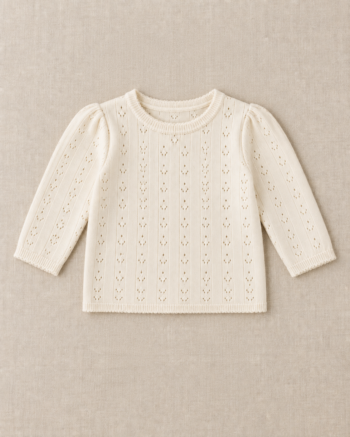 Cream pointelle knit long sleeve top with a ribbed crew neck, ribbed cuffs and a straight scalloped hem, laid flat on a linen surface.